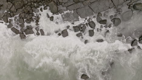 Close-aerial-footage-top-down-of-ocean-waves-crashing-into-rocks