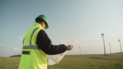 an engineer in a reflective vest stands with design plans at a wind farm