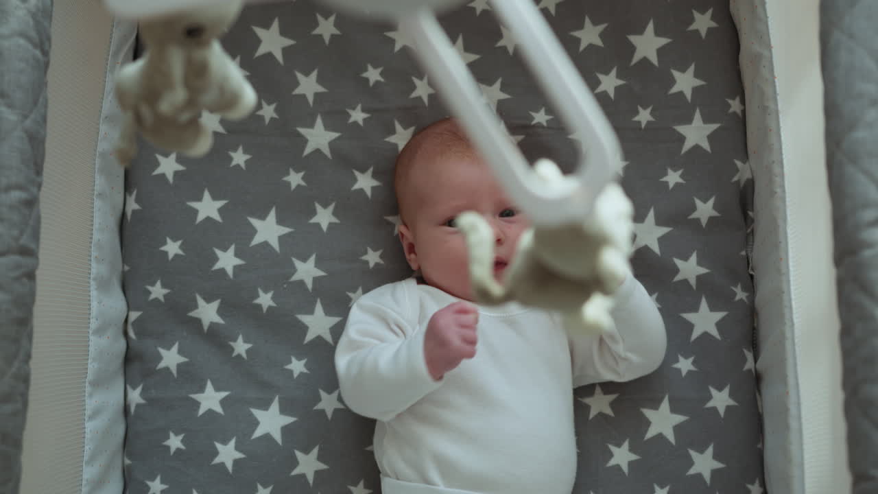 Neonato che riposa nella culla con biancheria da letto a fantasia stellata e giostrina sopra.