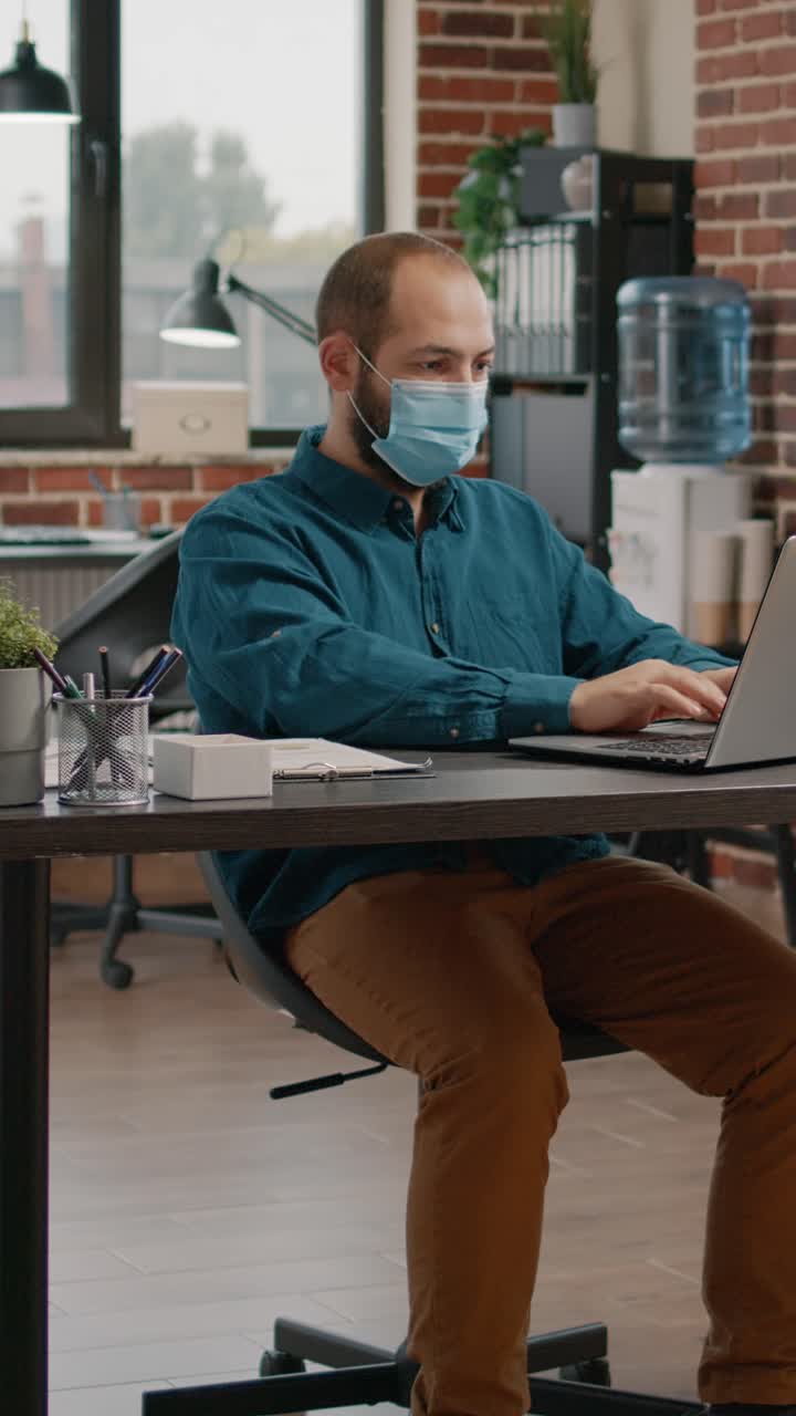 Man working on a computer with a face mask in an office workspace