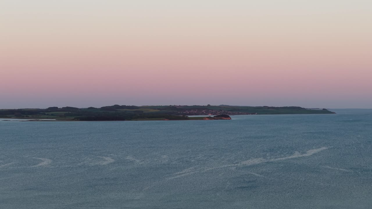 Luftfoto af et roligt hav og kystøer i tusmørket med bløde pastelfarver på himlen, der blander pink og blå over horisonten