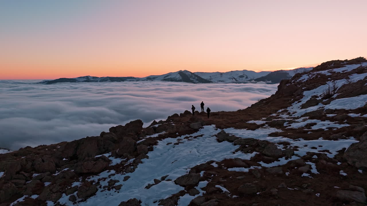 Due escursionisti si godono l'alba su una cima montuosa innevata sopra le nuvole, atmosfera pacifica.