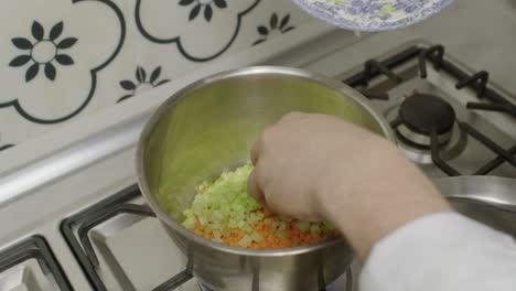 Adding diced celery into cooking pot with diced carrots