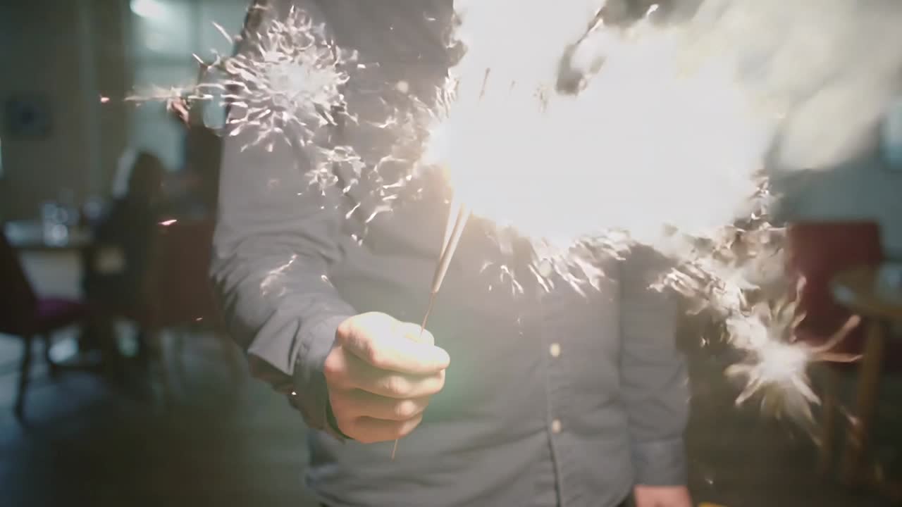 Uomo con una camicia scura che tiene e dirige una stellina luminosa in un salone in penombra, producendo pennacchi di fumo.