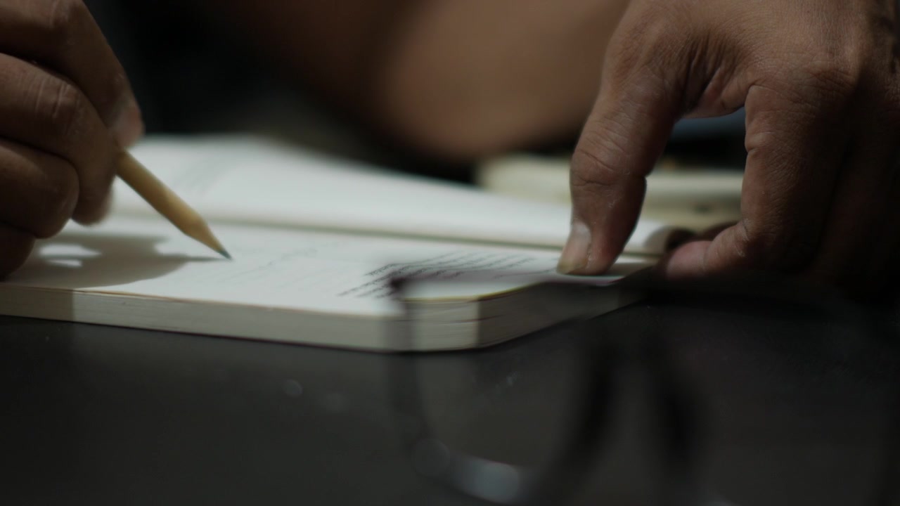 Person Writing in Notebook at Desk with Pencil