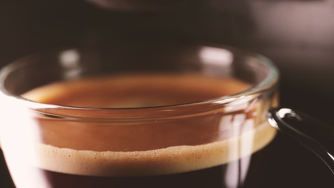 Drop of coffee falling into glass cup. Close-up