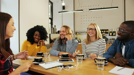 group multiethnic group of friends talking and laughing sitting at a table in a cafe