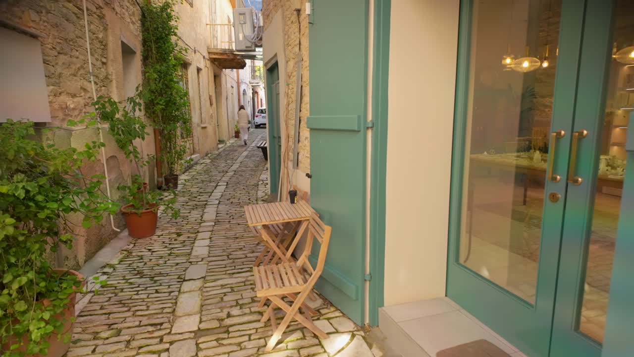 Una strada affascinante e acciottolata in un villaggio tradizionale con muri in pietra, piante in vaso e un piccolo tavolo in legno con sedie a Lefkara, Cipro. L'atmosfera serena è esaltata dalla calda luce del sole.