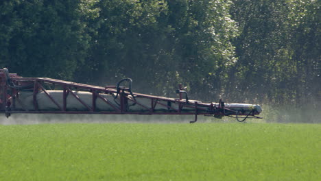 crops on farm land being sprayed by boom arm of sprayer tractor, tele shot