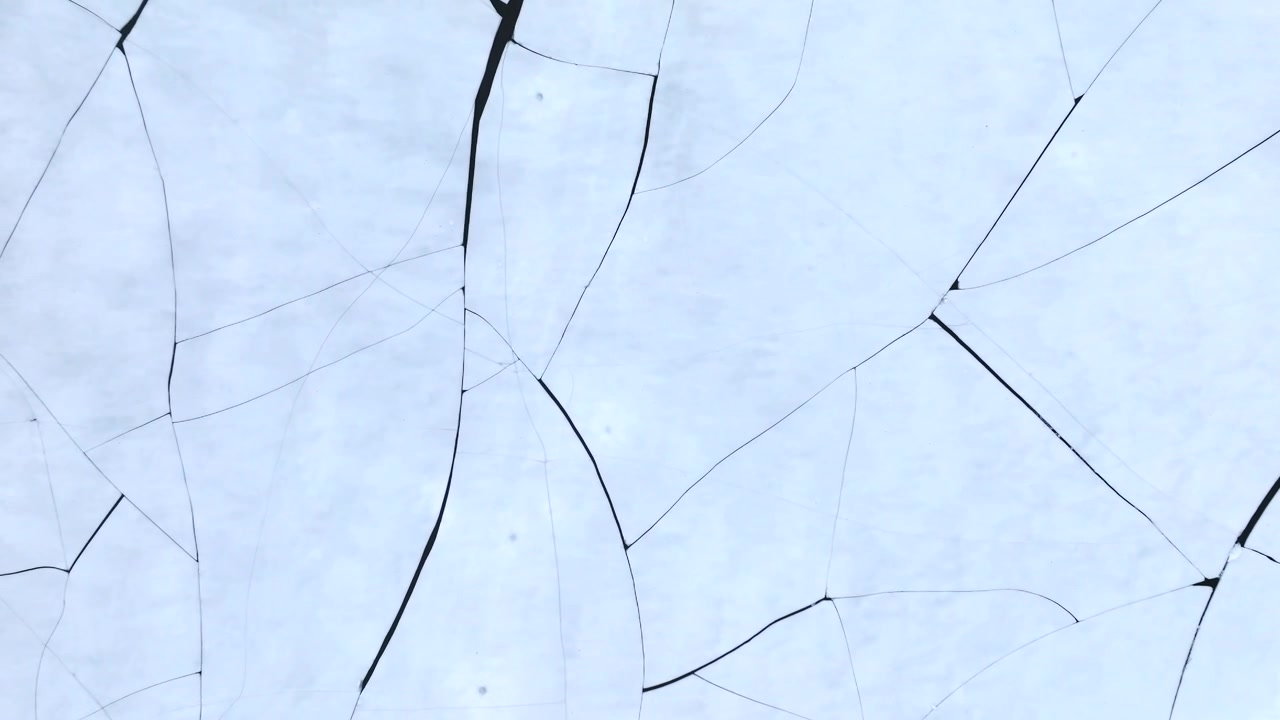 Stortvatnet lake on Austvagoya in Vagan Nordland Norway reveals thermal contraction cracks forming polygonal ice pattern with subtle surface reflection as drone rises from macro to close view