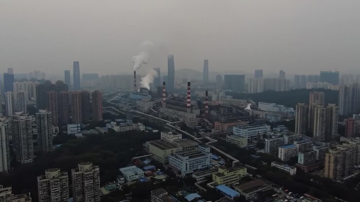 Aerial View of Industrial Cityscape: Smoke-emitting Chimneys and Urban Skyline Highlight the Sprawling Factory Complex Amidst Smoggy Atmosphere