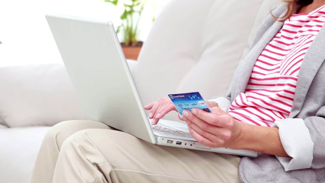 소파 위에 신용카드와 노트북을 가진 웃는 여자