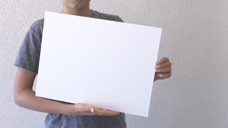 boy holding in his hands blank empty white mock up board poster. grey wall on background. close up