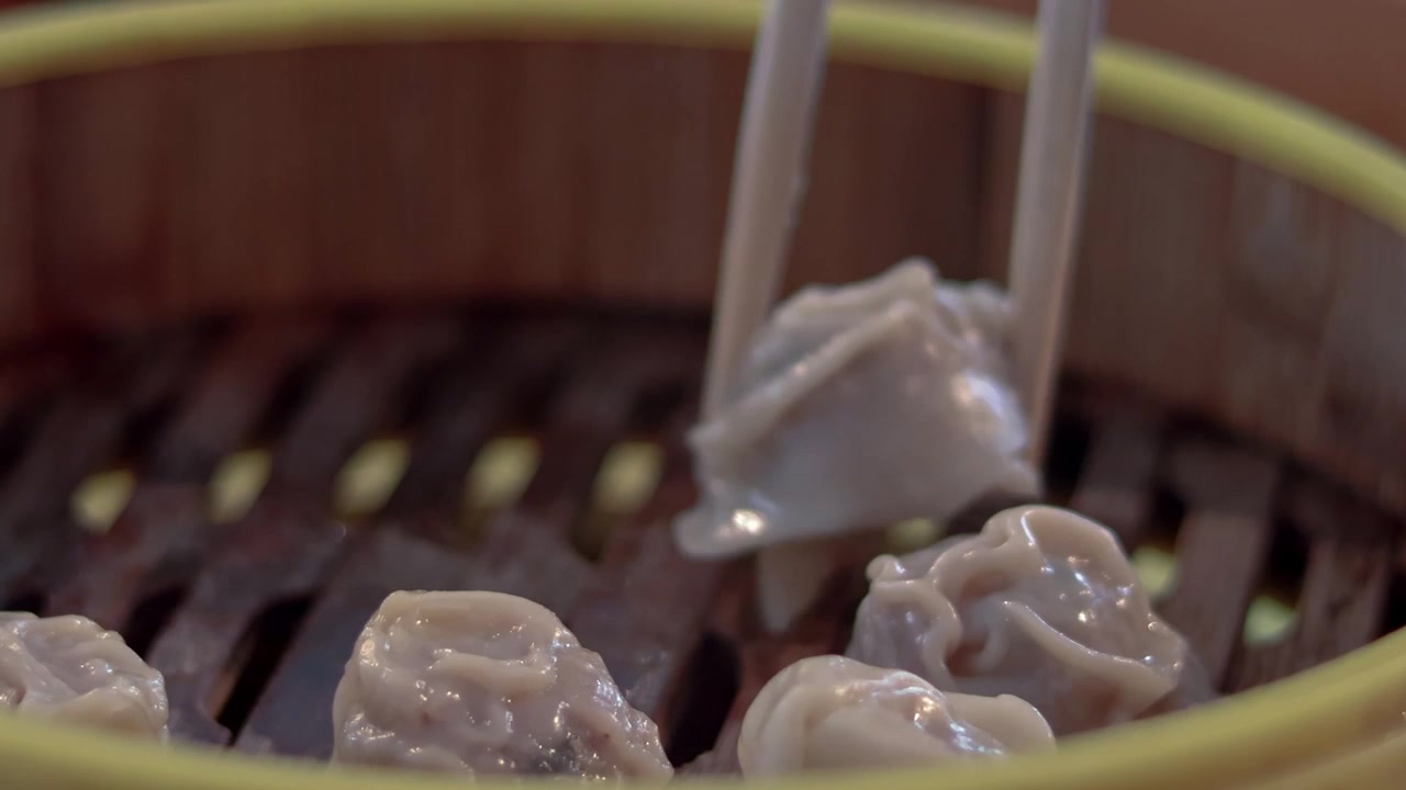 Plano de detalhe, pegando um har gow ou bolinho de camarão fumegante de uma cesta de bambu, um bolinho cantonês tradicional servido como dim sum