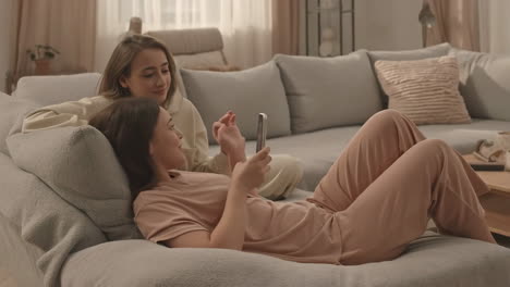 two women relaxing on a couch using a phone