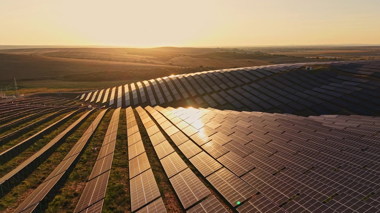 Udsigt ved solnedgang over solpaneler, der reflekterer sollys på en bakkeskråning i et landområde