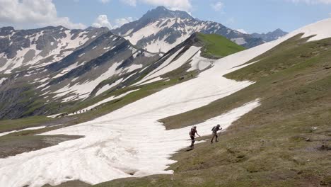 hikers walk up snow-covered mountain trails in the mont blanc alps, surrounded by dramatic peaks, aerial pullback