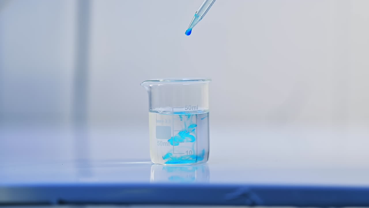 Beaker with water is placed on the laboratory table. A few drops of blue liquid are poured into the water. The examination of diapers process.
