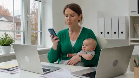 mother on phone with baby in green cardigan, office