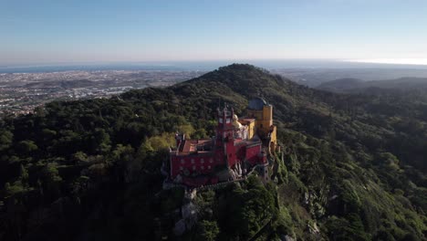cinematic drone shot circling around historic pena palace castle standing a top of a hill in sintra mountains above town of sintra, portugal