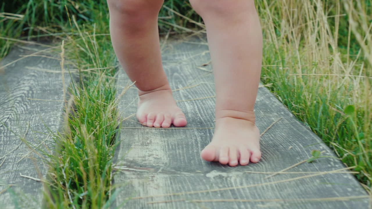 las piernas del bebé dan los primeros pasos vacilantes a lo largo del camino de madera entre la hierba primer éxito
