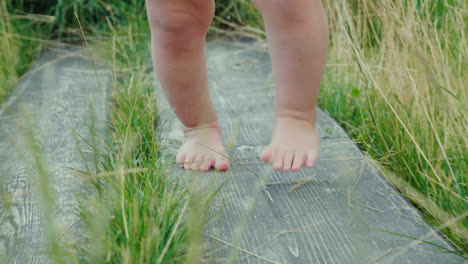 Die-Beine-Des-Babys-Machen-Die-Ersten-Unsicheren-Schritte-Auf-Dem-Holzweg-Im-Gras-Erster-Erfolg