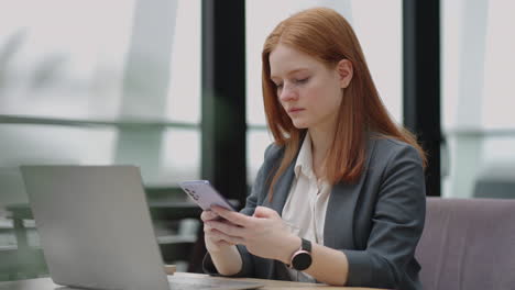 Beautiful-young-business-woman-using-phone-in-office.-Woman-using-a-smartphone-and-leaning-on-a-window-texting-sending-emails-planning-meetings-networking-online-browsing-messages-on-mobile-phone