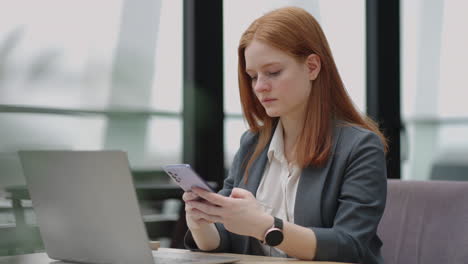 Hermosa-Joven-Mujer-De-Negocios-Usando-El-Teléfono-En-La-Oficina.-Mujer-Usando-Un-Teléfono-Inteligente-Y-Apoyada-En-Una-Ventana-Enviando-Mensajes-De-Texto-Enviando-Correos-Electrónicos-Planificando-Reuniones-Haciendo-Contactos-En-Línea-Navegando-Mensajes-En-Un-Teléfono-Móvil