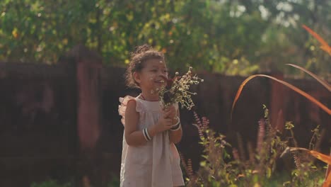 Toma-Estática-De-Mano-De-Una-Niña-Que-Se-Ríe-En-El-Jardín-Mientras-Sostiene-Un-Ramo-De-Flores-En-Sus-Manos-Con-Plantas,-árboles-Y-Una-Pared-De-Piedra-En-El-Fondo