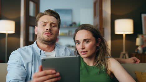 una pareja conmocionada mirando fijamente un dispositivo digital en el hogar. los cónyuges examinan la tableta.