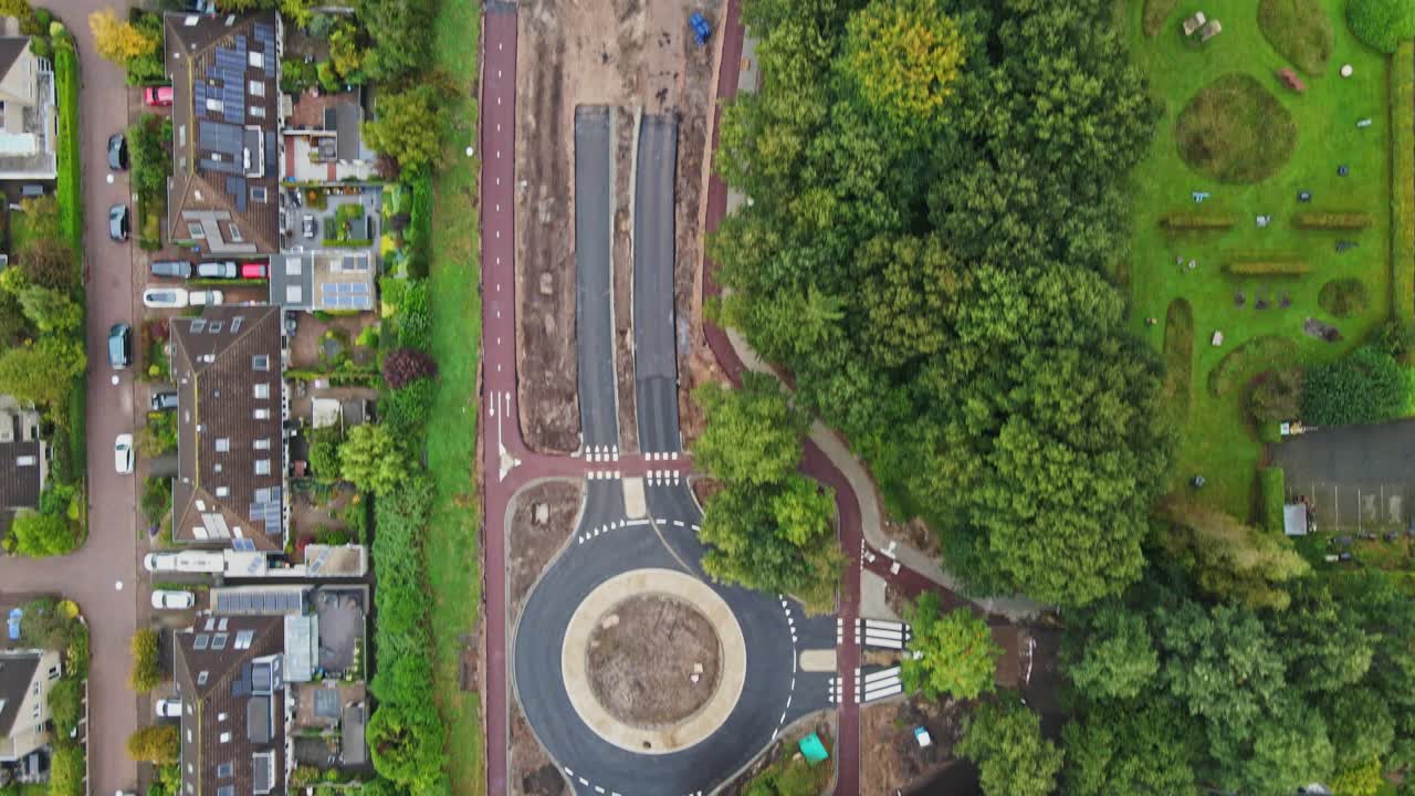 Beautiful top down aerial of a new road and roundabout being constructed in a small town with a lot of green trees and parks