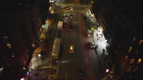 Forwards-tracking-of-typical-yellow-cab-driving-through-streets-of-night-city.-High-angle-view-of-taxi-passing-road-intersection.-Manhattan,-New-York-City,-USA