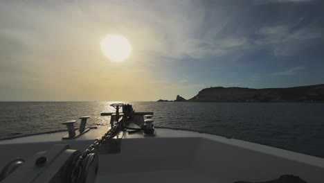 point of view of sailboat bow navigating toward corsica island cliffs and capo pertusato lighthouse in france with sun in background at sunset, slow motion