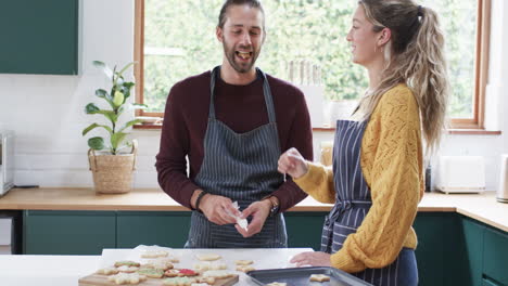 Happy-diverse-couple-decorating-christmas-cookies-in-kitchen-at-home,-in-slow-motion