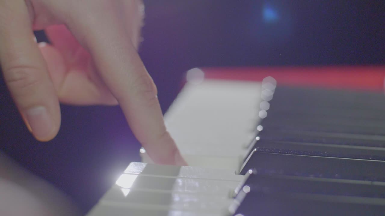Close up of a keyboard players hands playing on an electric stage piano synthesizer keyboard. Backward dolly movement with stage light scenery going out of focus. Shot in 4K at 120fps.