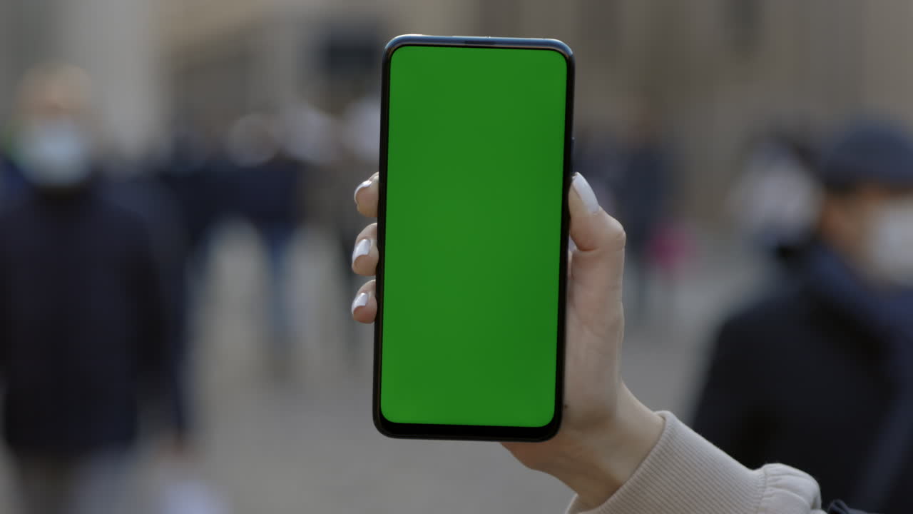 Person holding a phone with a green screen in a city