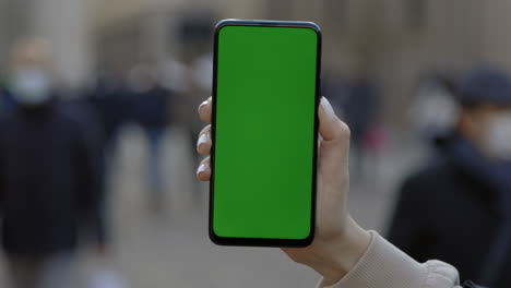 person holding a phone with a green screen in a city