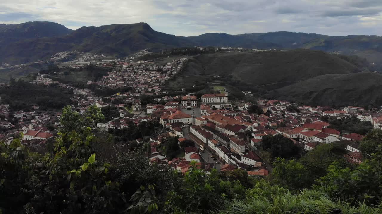 Aerial backward movement with historic colonial city of Ouro Preto in Minas Gerais, revealing the São Sebastião viewpoint sign [San Sebastian Hill] with lookout point in the foreground