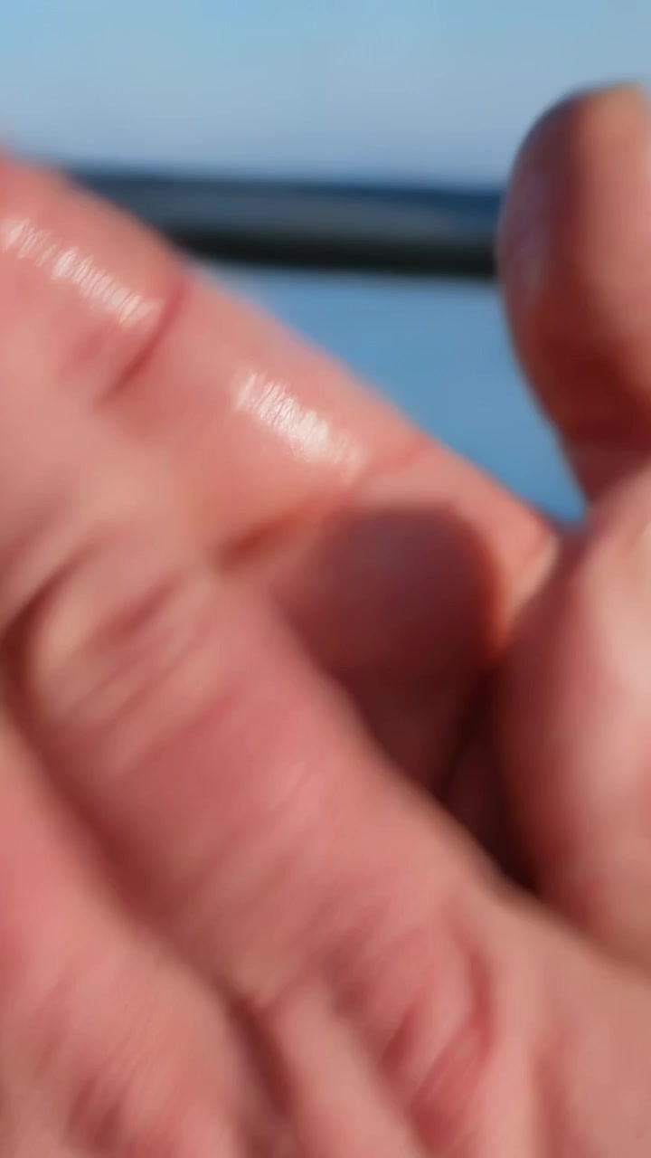 Vertical video: Reaching right hand shielding camera lens on deck by railing, prompted by sunlight