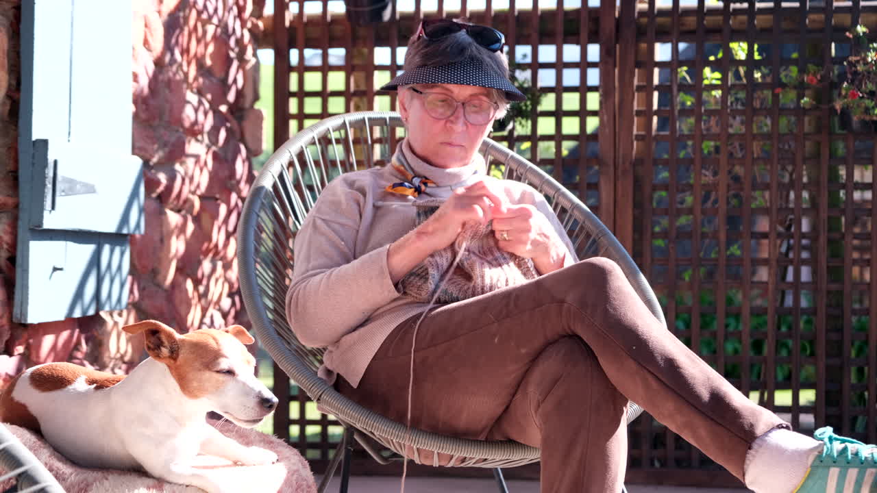 Grandma sit on sunny patio and knits with cute Jack Russell companion dog nearby