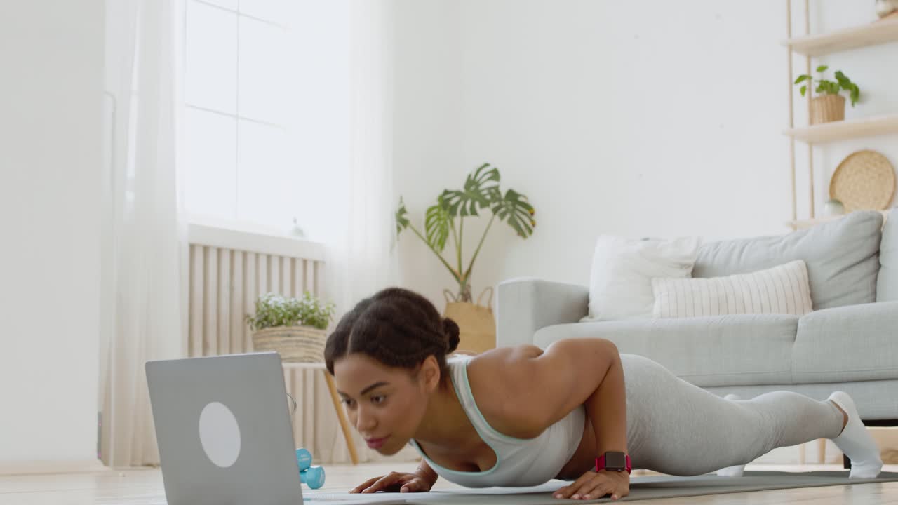 mujer haciendo un ejercicio de tabla en casa, siguiendo un video de fitness en línea
