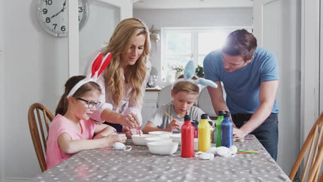 Padres-Con-Niños-Con-Orejas-De-Conejo-Sentados-A-La-Mesa-Decorando-Huevos-De-Pascua-En-Casa.