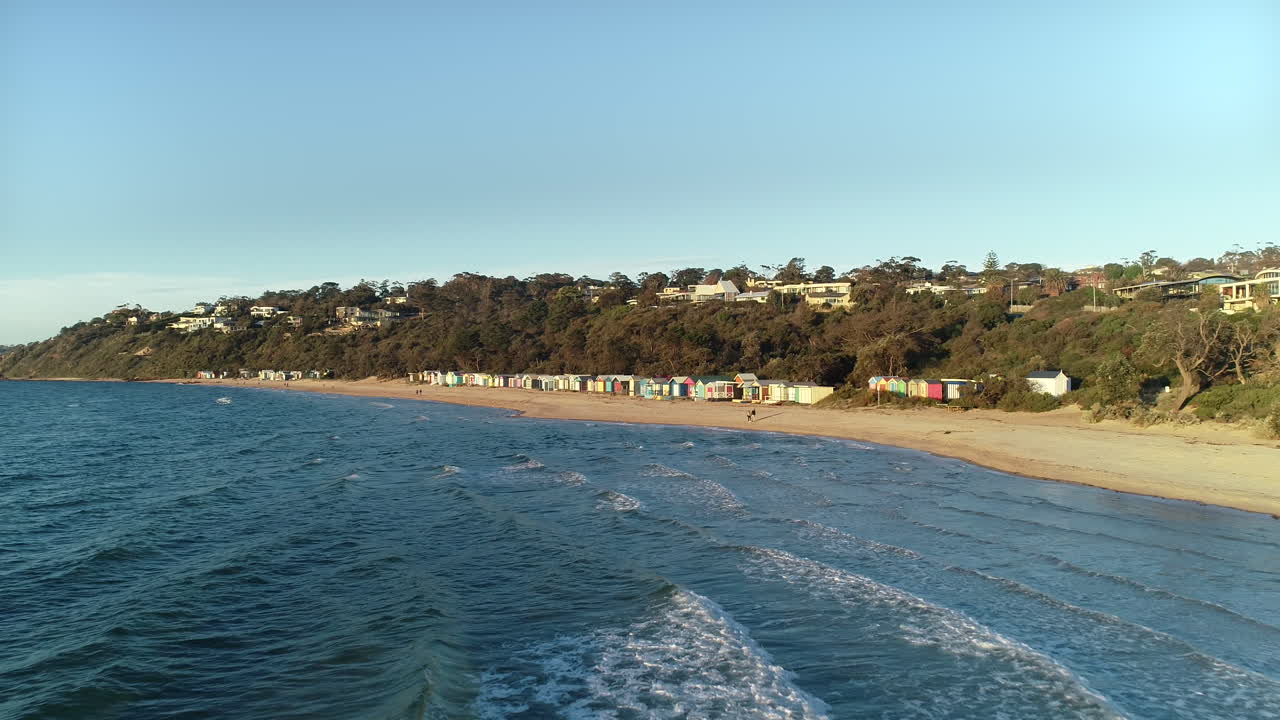 seguimiento de la perspectiva aérea hacia las cajas de la playa de mornington mientras la pareja camina a lo largo de la costa