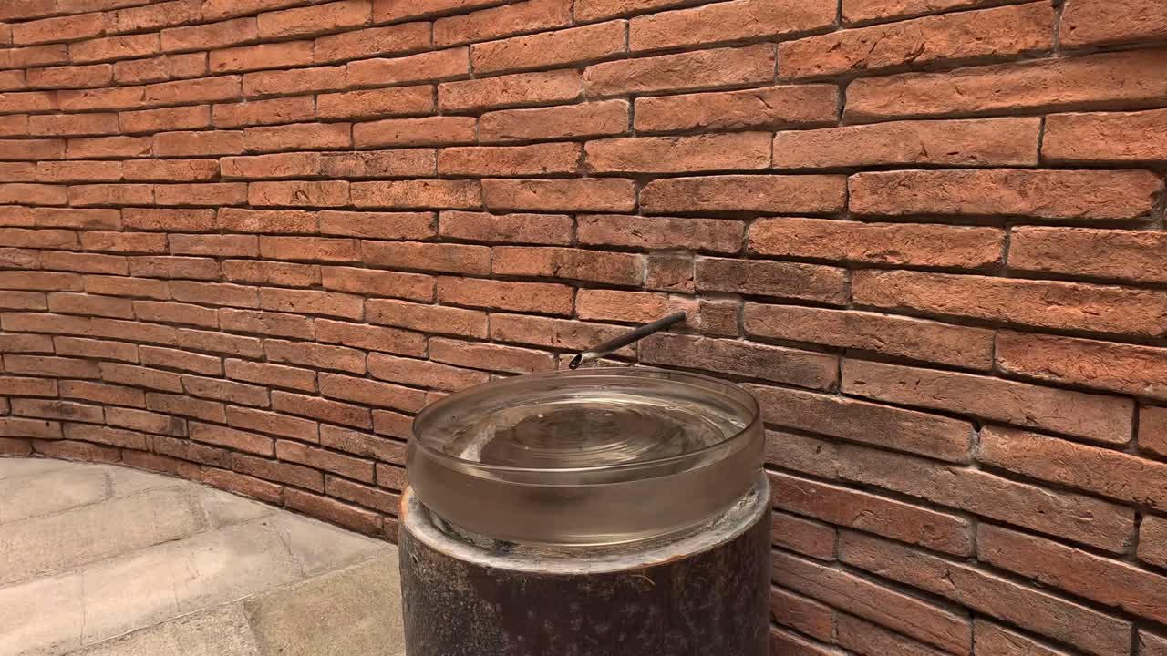 Un barattolo di vetro che trabocca d'acqua contro un muro di mattoni