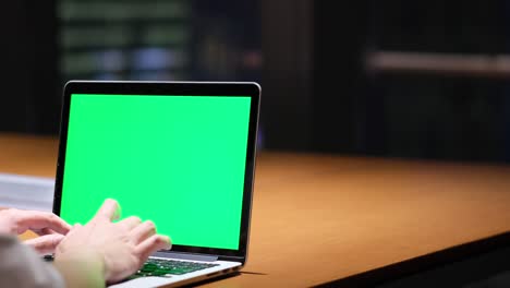 hand typing green screen laptop computer in office at night