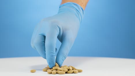 guantes azules de mano de primer plano recogiendo una tableta de suplemento de zinc marrón, toma de estudio