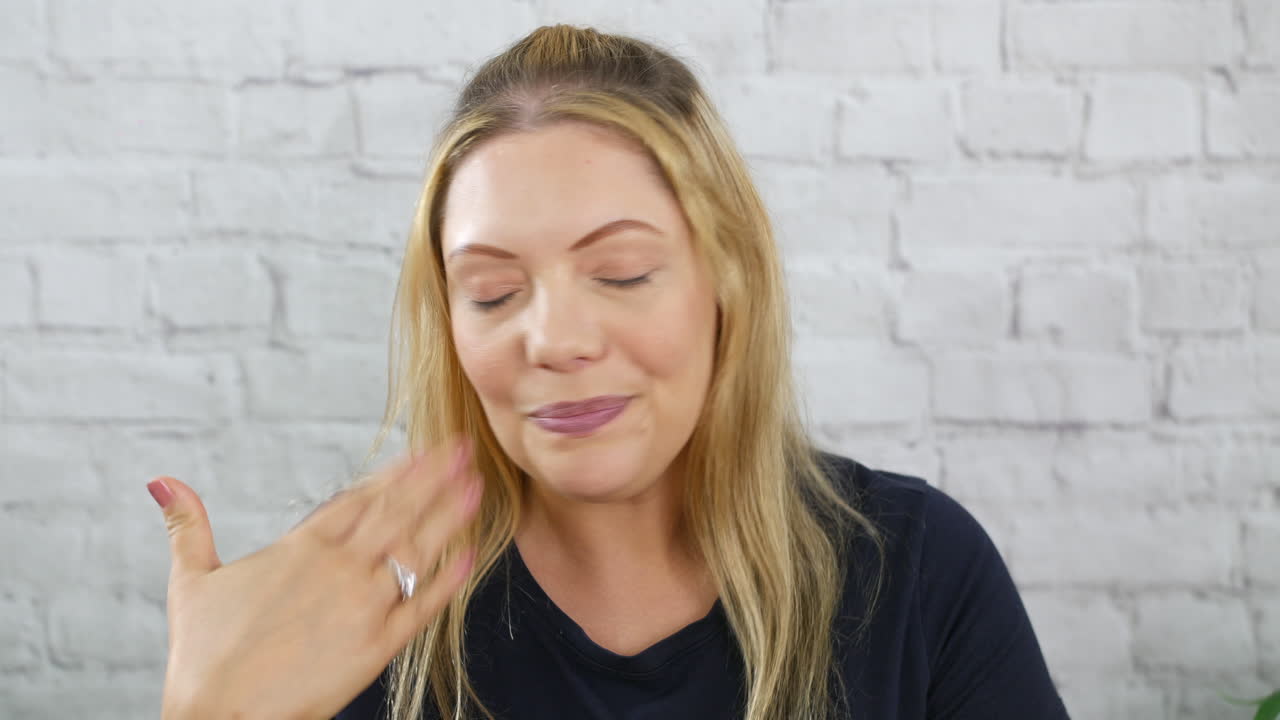 una mujer rubia caliente, molesta y nerviosa con un flujo de calor contra una pared de ladrillo blanco