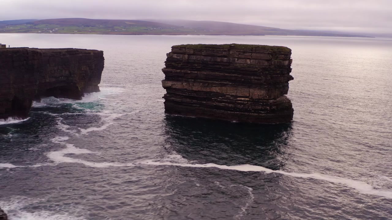 Aerial push in reveals Dun Briste sea stack off Downpatrick Head cliffs in Ireland, wide view under cloudy sky