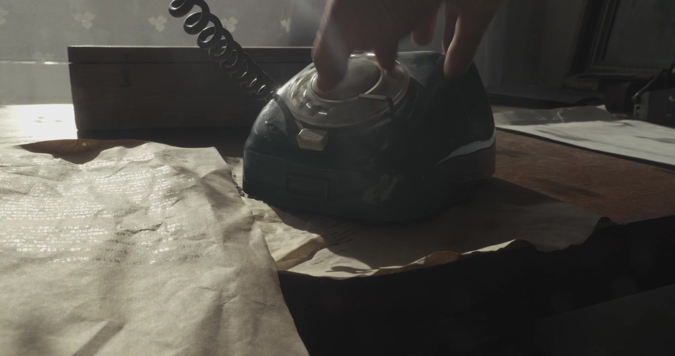 Lavvinklet iscenesat optagelse der glider hen over krøllede, gamle dokumenter, før den afslører en person der ringer på en retro bordtelefon på et kontor