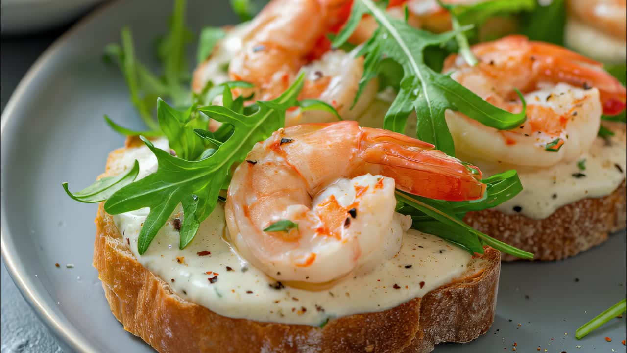 Close up of two slices of toasted bread topped with creamy sauce, seasoned shrimp, and fresh arugula, creating an inviting appetizer or snack